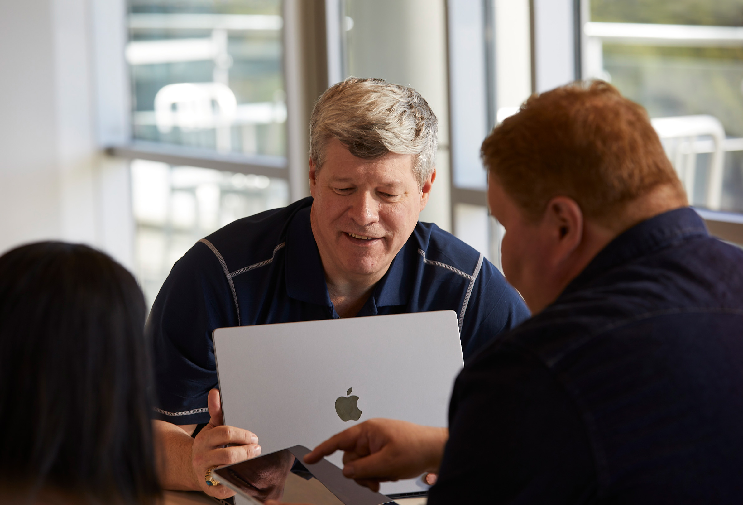 ثلاثة موظفين في Apple يستخدمون MacBook وiPad للتعاون في إنجاز العمل.
