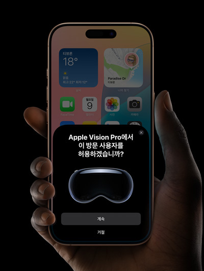 iPhone을 들고 있는 손. iPhone 화면에 “Apple Vision Pro에서 이 방문 사용자를 허용하겠습니까?”라는 메시지와 함께 “계속” 및 “거절” 버튼이 표시된 창의 모습.