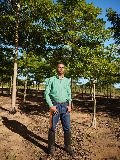 Victor Leon Rocha Araújo porte des bottes hautes et se tient dans une rangée d’arbres de la forêt atlantique.