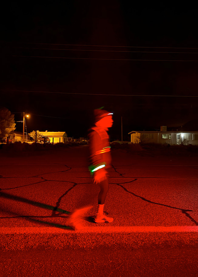 Ảnh chụp một vận động viên chạy bộ trong bóng tối mặc đồ phản quang trên đường.