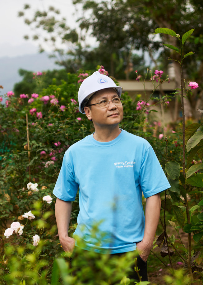 Foto van Phan Viet Dung, die buiten met een veiligheidshelm op tussen de bloemen staat.