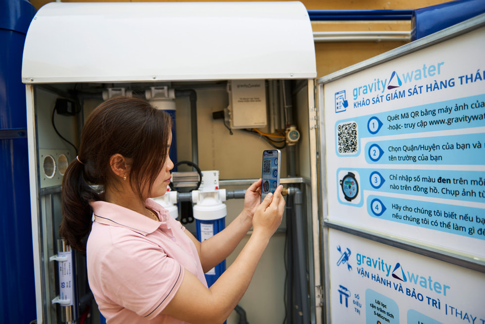 A student holds up an iPhone device to scan a QR code on Gravity Water signage at the Vầy Nưa Primary and Secondary Boarding School for Ethnic Minorities.