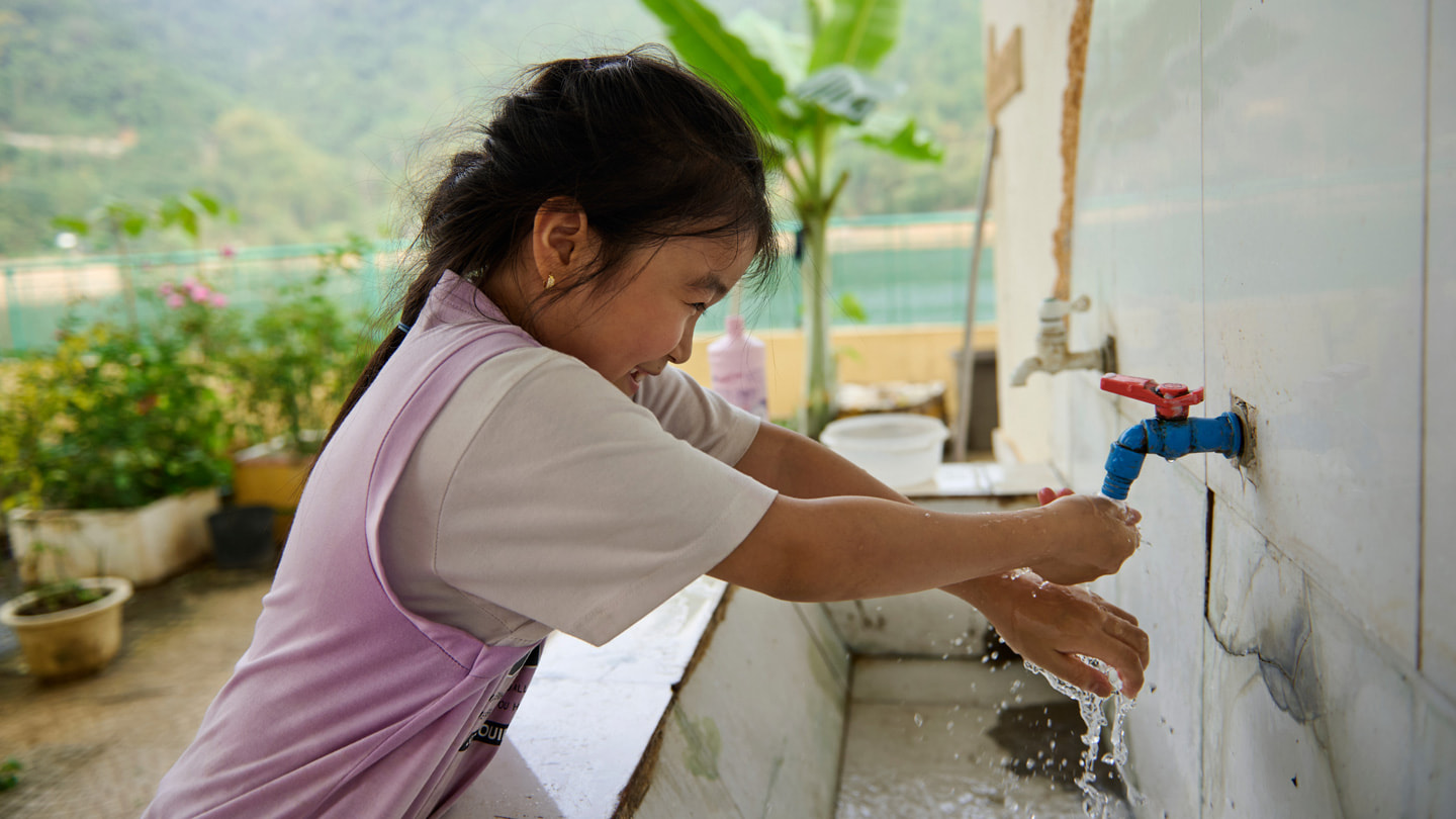 Een leerling van de school voor basis- en middelbaar onderwijs in Hiền Lương wast buiten haar handen onder de kraan boven een grote wasbak.
