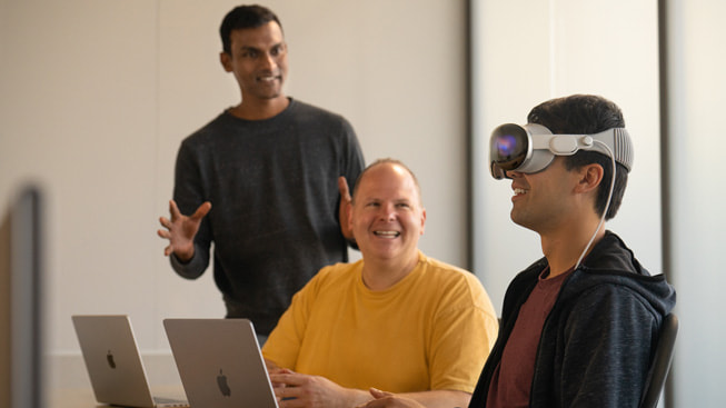Afbeelding van een ontwikkelaar die Apple Vision Pro aan het testen is, terwijl twee andere ontwikkelaars toekijken.