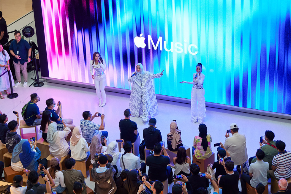 Aufnahme von De Fam beim Auftritt für Kund:innen mit dem Apple Music Logo auf dem Bildschirm hinter ihnen.
