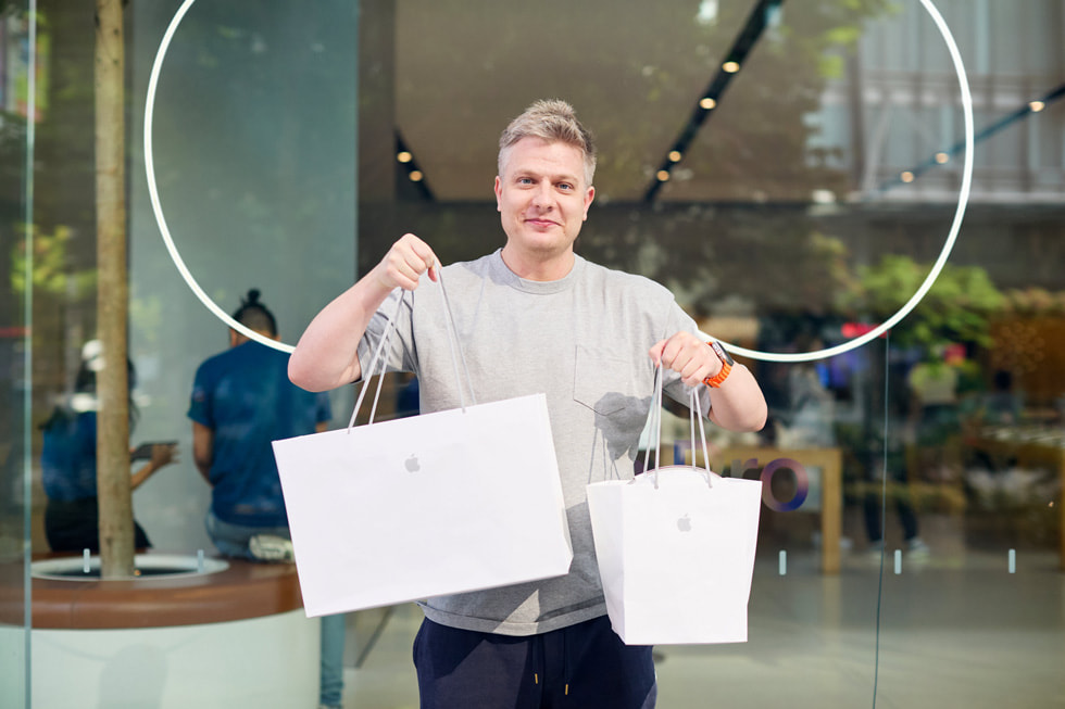 A customer holds up two Apple bags containing his new purchases.