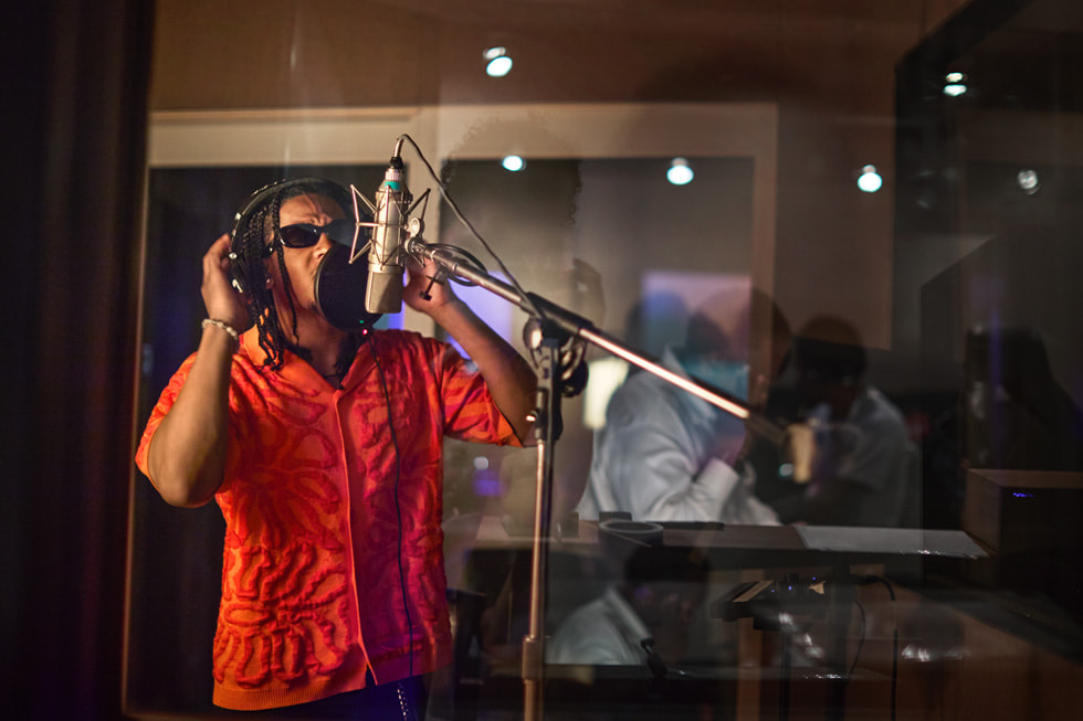 Emmanuel Strickland 戴著耳機，在錄音室環境中對著專業麥克風唱歌。