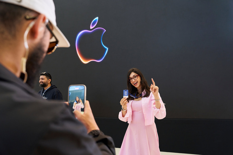 Un integrante del equipo de Apple fotografía a un asistente que posa con su insignia de la WWDC24. 