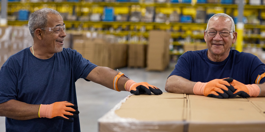 Empleados usando guantes y gafas de seguridad junto a un palé de cajas en un almacén
